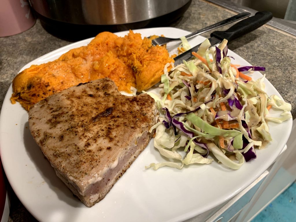 Photo of Tuna Steaks, Sweet Potatoes, and slaw on a white plate with a fork and a knife on the side. 